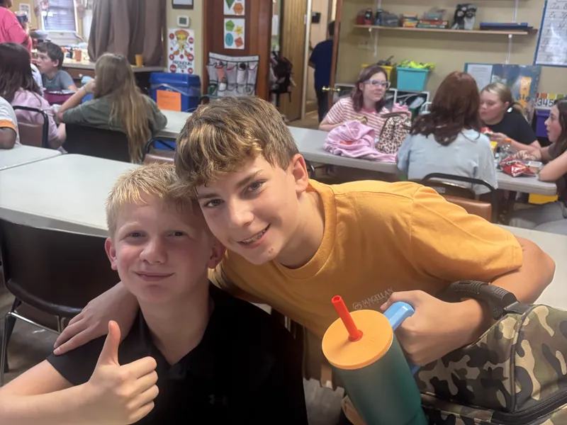 Two students giving a thumbs up at a classroom table