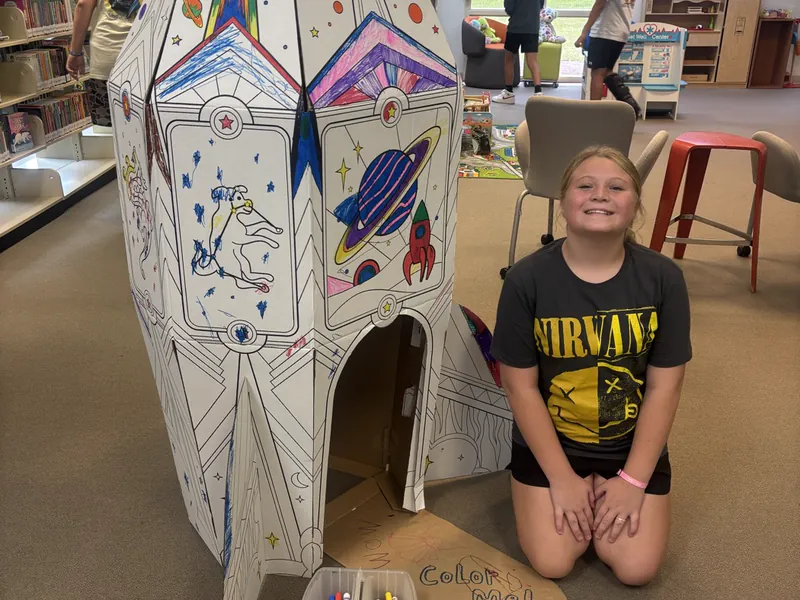 A student with a large cardboard castle made in class