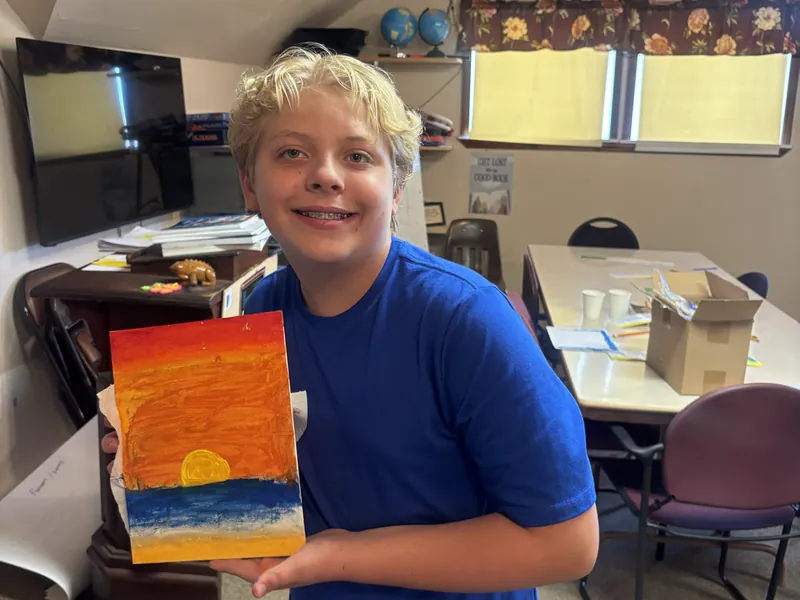 A student holding up a sunset painting