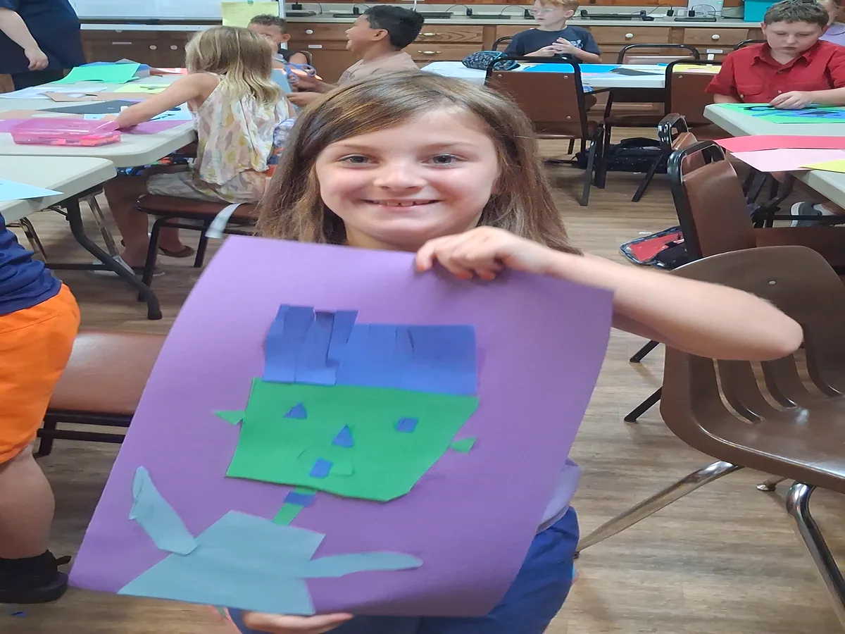 A student holding up a cut-paper house made in art class